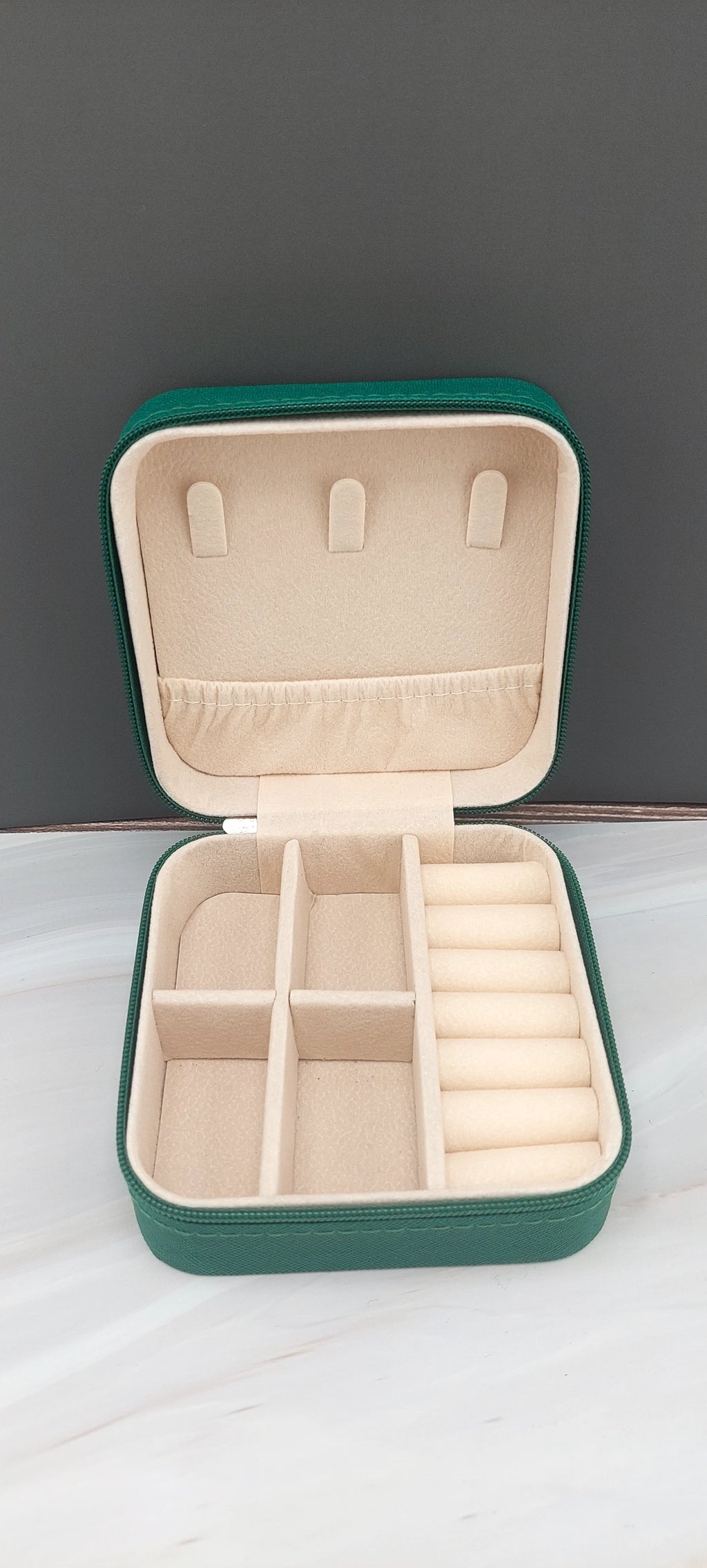 A square jewelry box made of black material with a beige interior, featuring compartments for organizing jewelry.