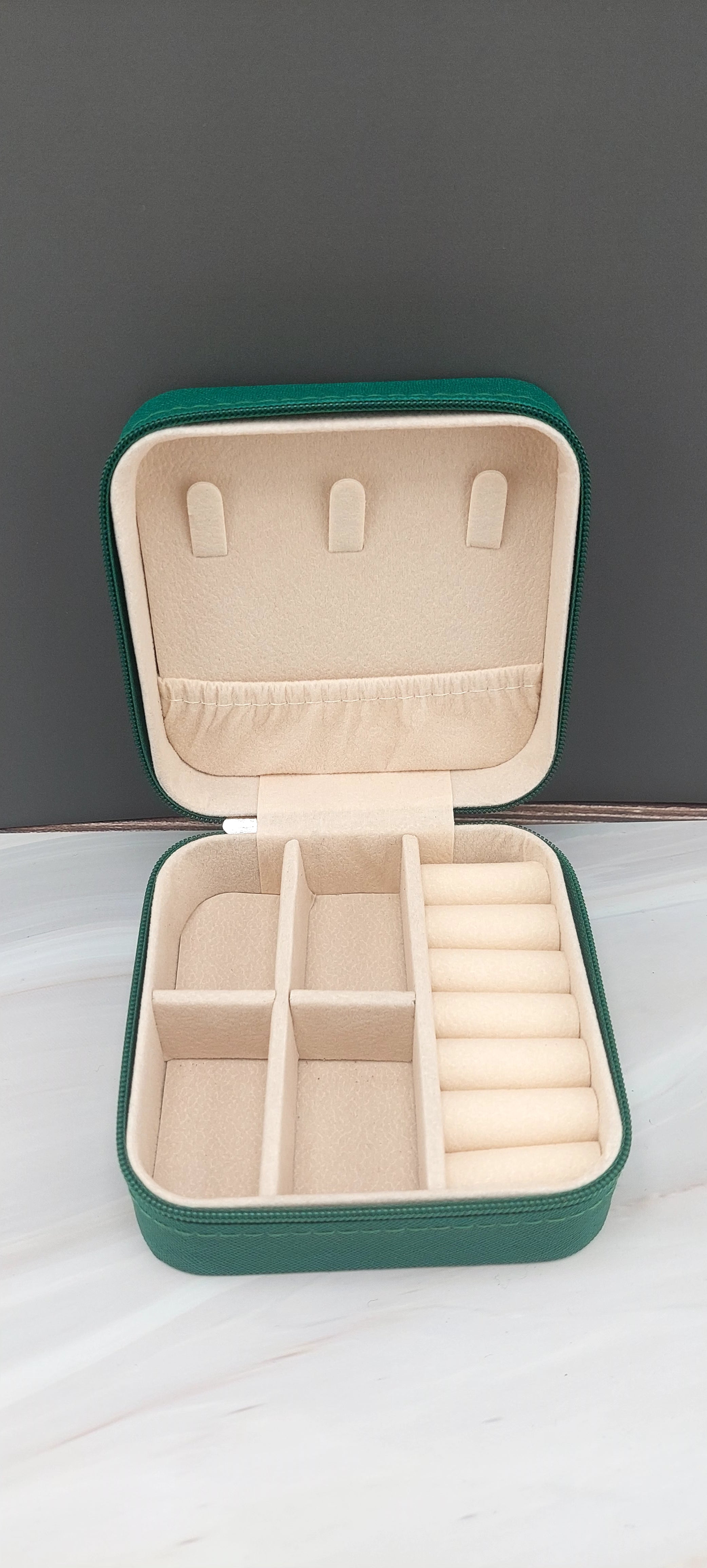 A square jewelry box made of black material with a beige interior, featuring compartments for organizing jewelry.