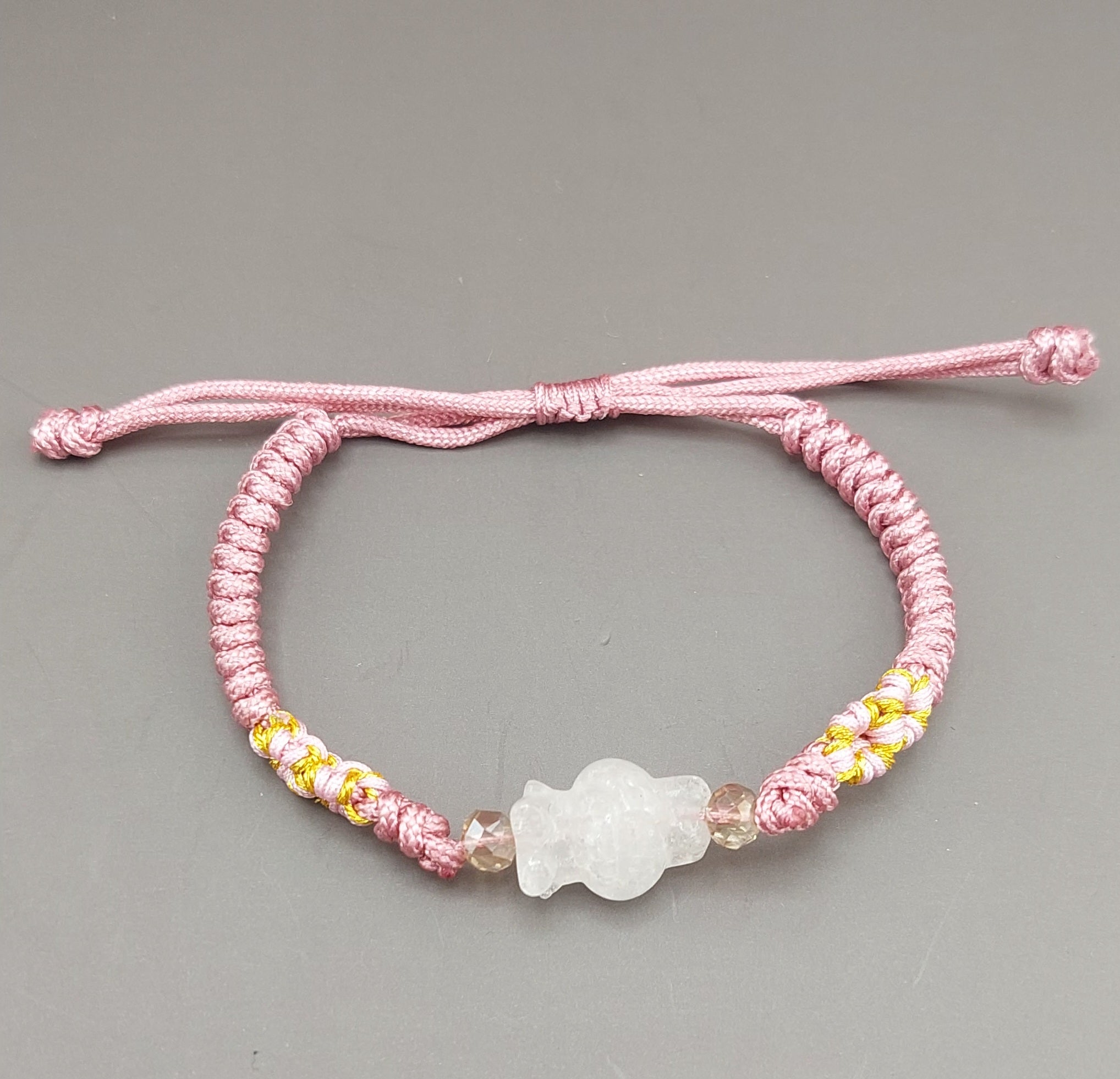 A pink and yellow bracelet with a white floral charm, displayed against a grey background