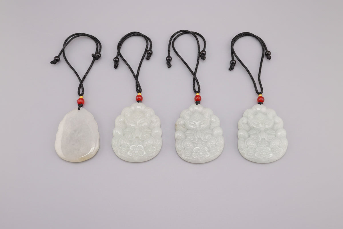 Three carved jade pendants with floral and cloud motifs, each on a black cord with red beads, displayed on a dark gray surface.