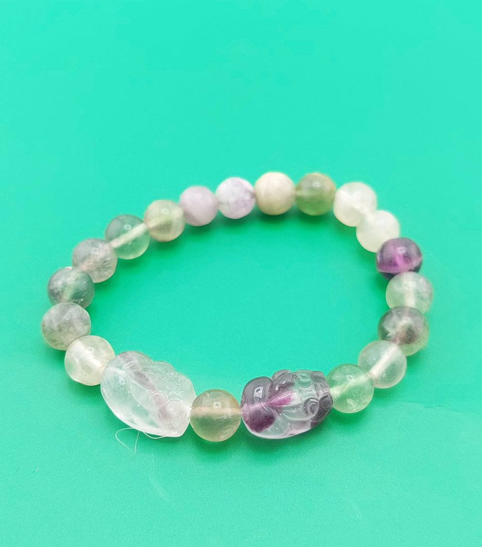 A multicolored fluorite pixiu bracelet displayed against a green background.