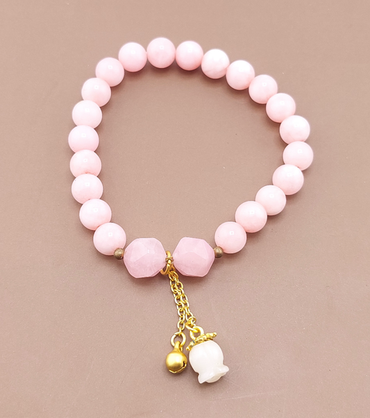 A pink beaded bracelet with gold-colored metal accents and charms, displayed against a neutral background.