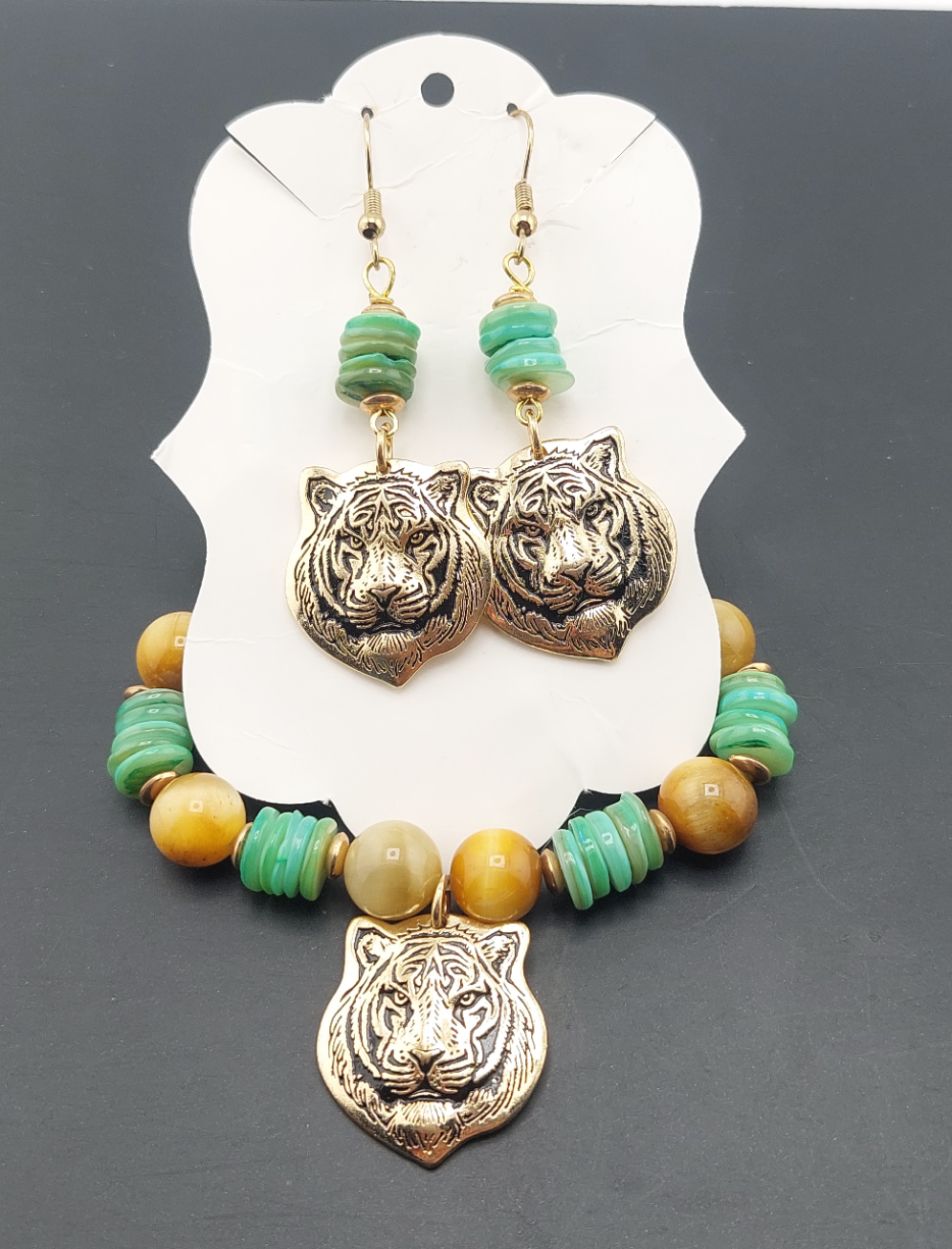 A set of jewelry featuring tiger charm pendants and tiger eye stones on a necklace and matching earrings, displayed on a white card.