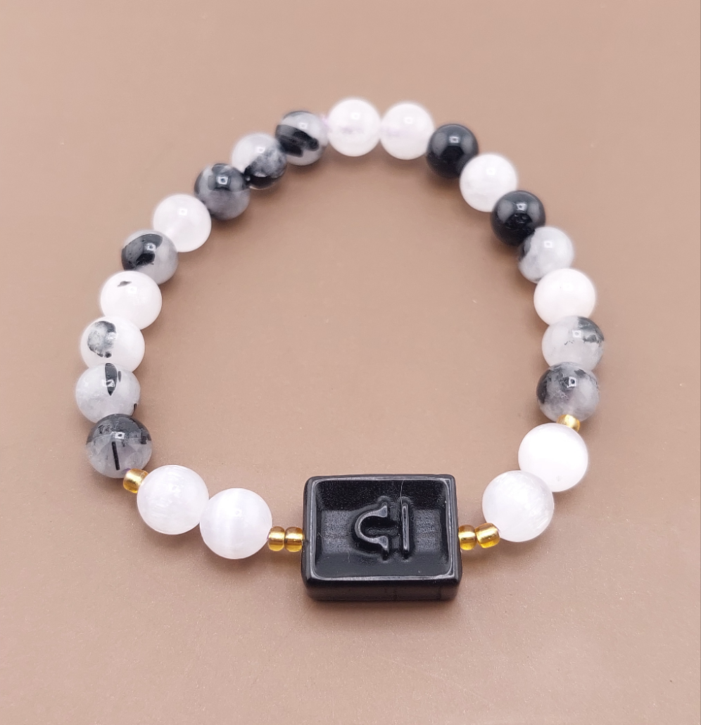 A beaded bracelet with round beads in shades of gray and pink, featuring a rectangular pendant with a zodiac symbol on it, displayed against an orange background.