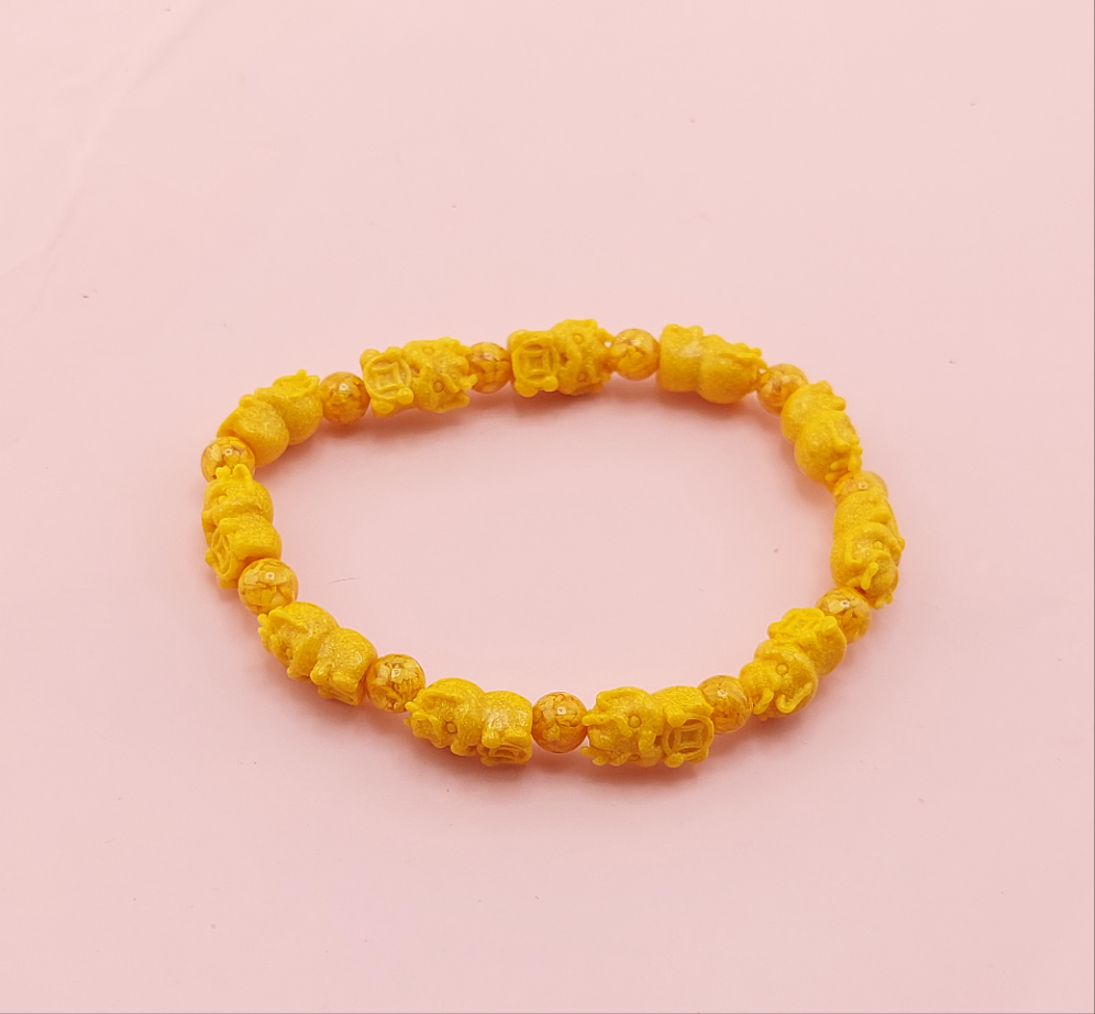 A yellow bracelet with skull designs on the beads, displayed against a pink background.