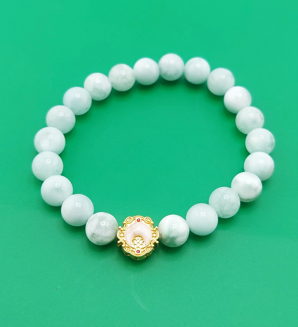 A bracelet with white beads and a gold-colored clasp, displayed against a green background.