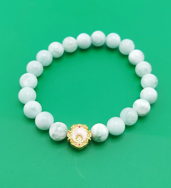 A bracelet with white beads and a gold-colored clasp, displayed against a green background.