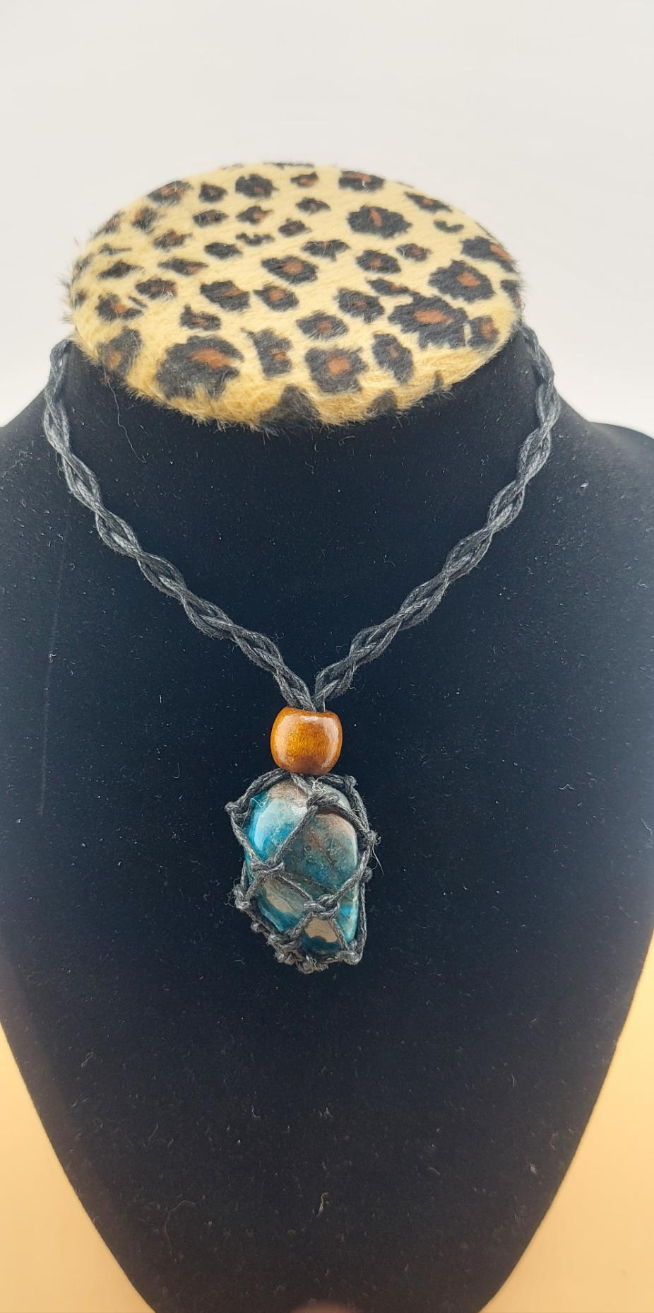 A black macrame necklace with a tumbled stone pendant displayed on a mannequin bust with a leopard print collar.