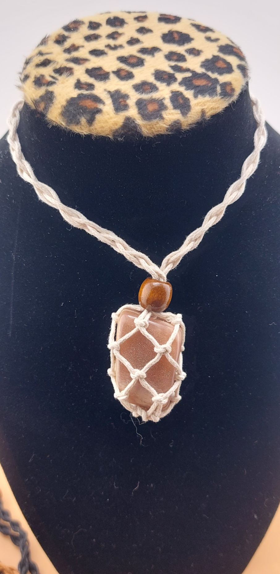 A sunstone macrame necklace with a tumbled stone pendant displayed on a mannequin bust with a leopard print collar.