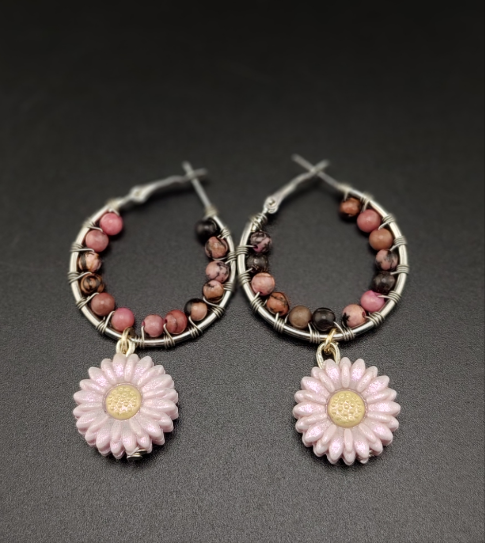 A pair of gold-colored hoop earrings with wire wrapping and white beads, featuring pink flower charms attached to the hoops.