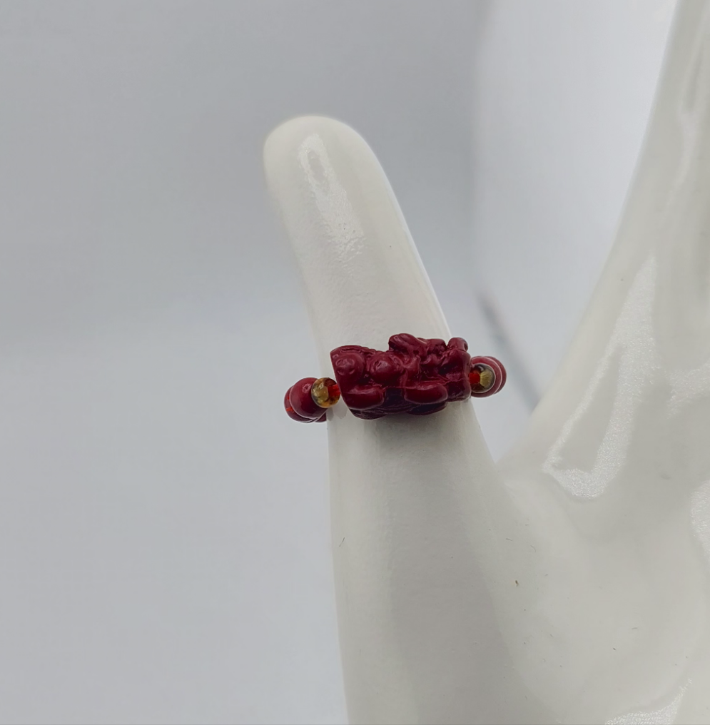 A red Pixui Cinnabar Dragon Ring displayed on a white stand.