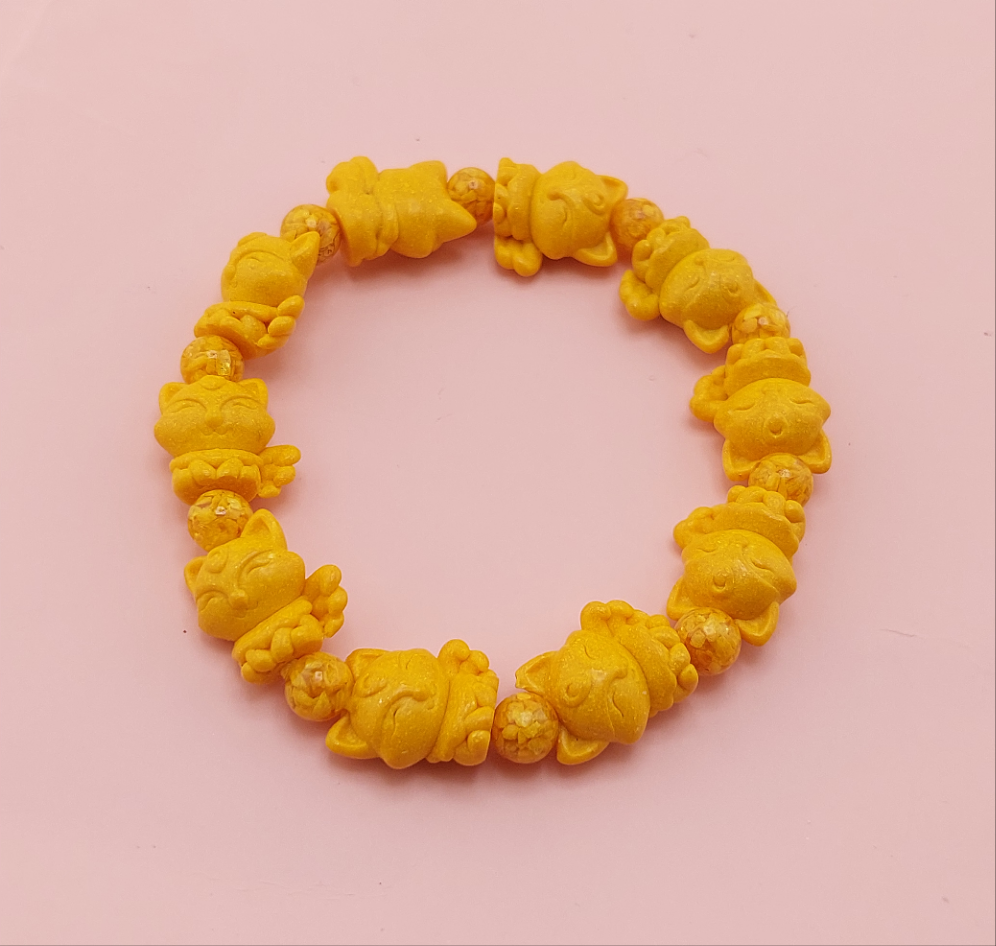 A yellow bracelet with skull designs on the beads, displayed against a pink background.