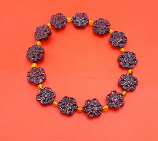 A bracelet with dark amber floral beads and yellow accent beads displayed against an orange background.