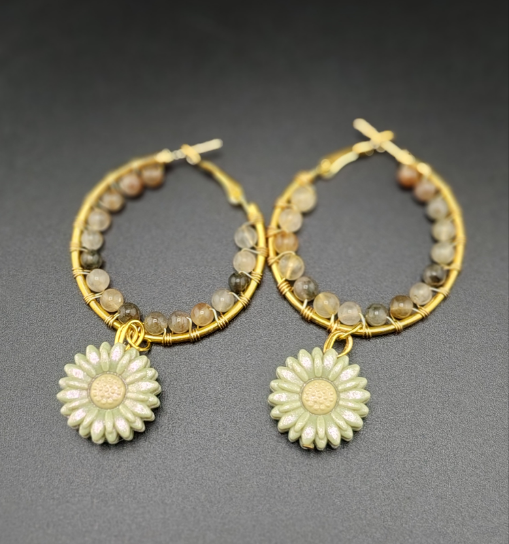 A pair of gold-colored hoop earrings with wire wrapping and white beads, featuring pink flower charms attached to the hoops.