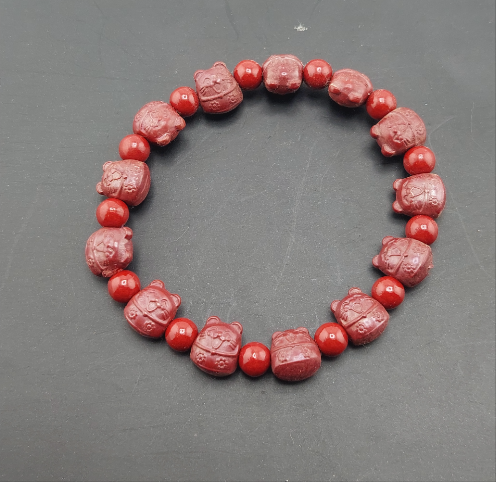A red cinnabar bracelet with decorative bead carvings displayed on a dark surface.