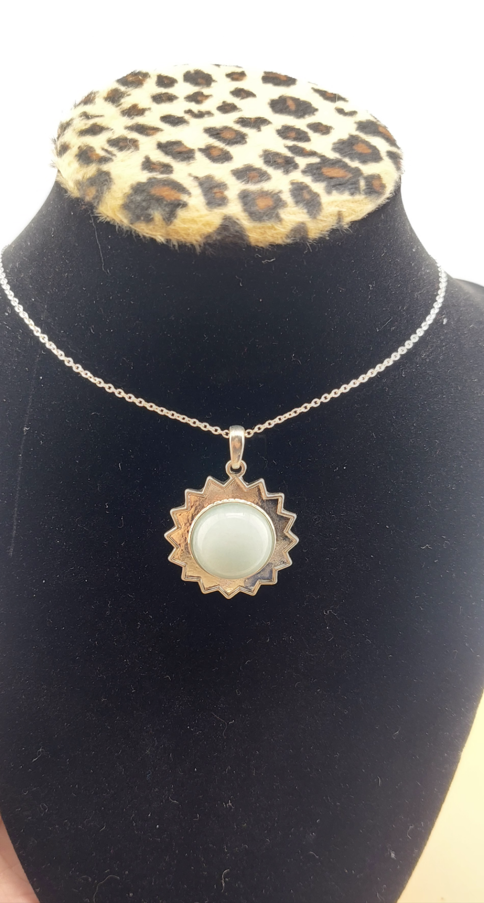 A gold-colored sun-shaped necklace displayed on a black mannequin with a leopard print collar.