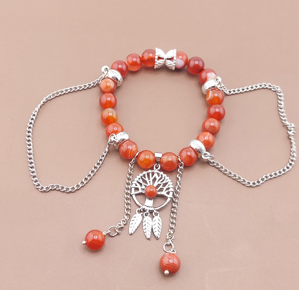 A silver-colored Tree of Life bracelet with orange carnelian beads and small silver pendants, displayed against a neutral background.
