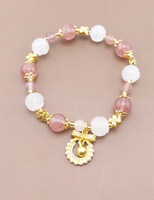 A gold-colored metal bracelet with white and pink beaded details, featuring a gold bow charm and a bell-shaped charm.