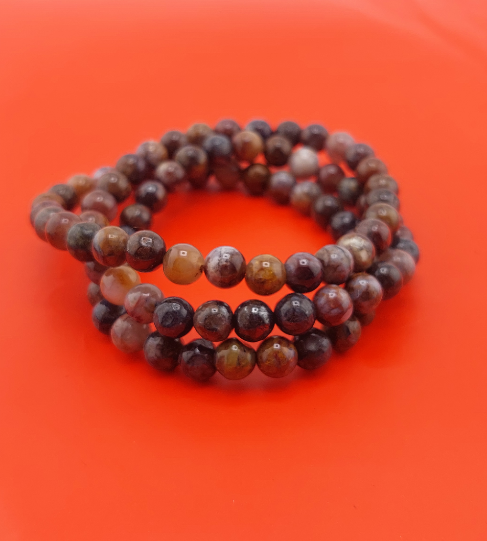 A triple bracelet with round beads in shades of red, orange, and white, displayed on a bright orange surface.