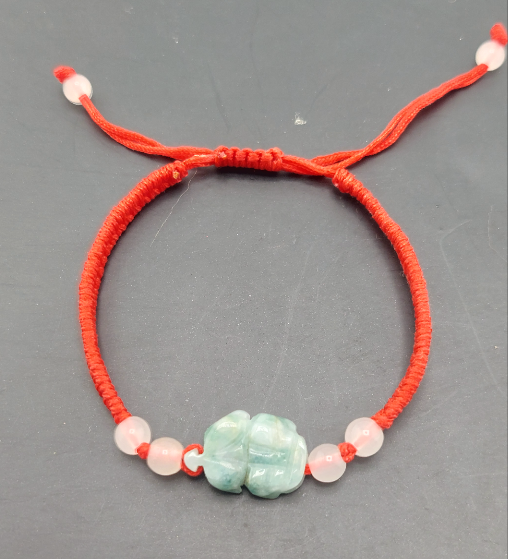 An adjustable bracelet with a red cord, featuring a green Pixui dragon charm and small white beads.