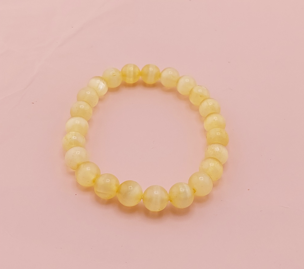 A yellow beaded bracelet on a pink background.