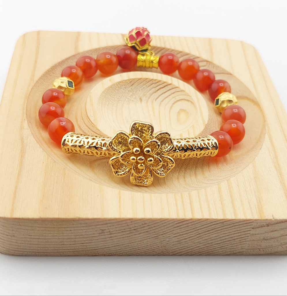 A gold-colored floral bracelet with orange carnelian beads displayed on a wooden surface.