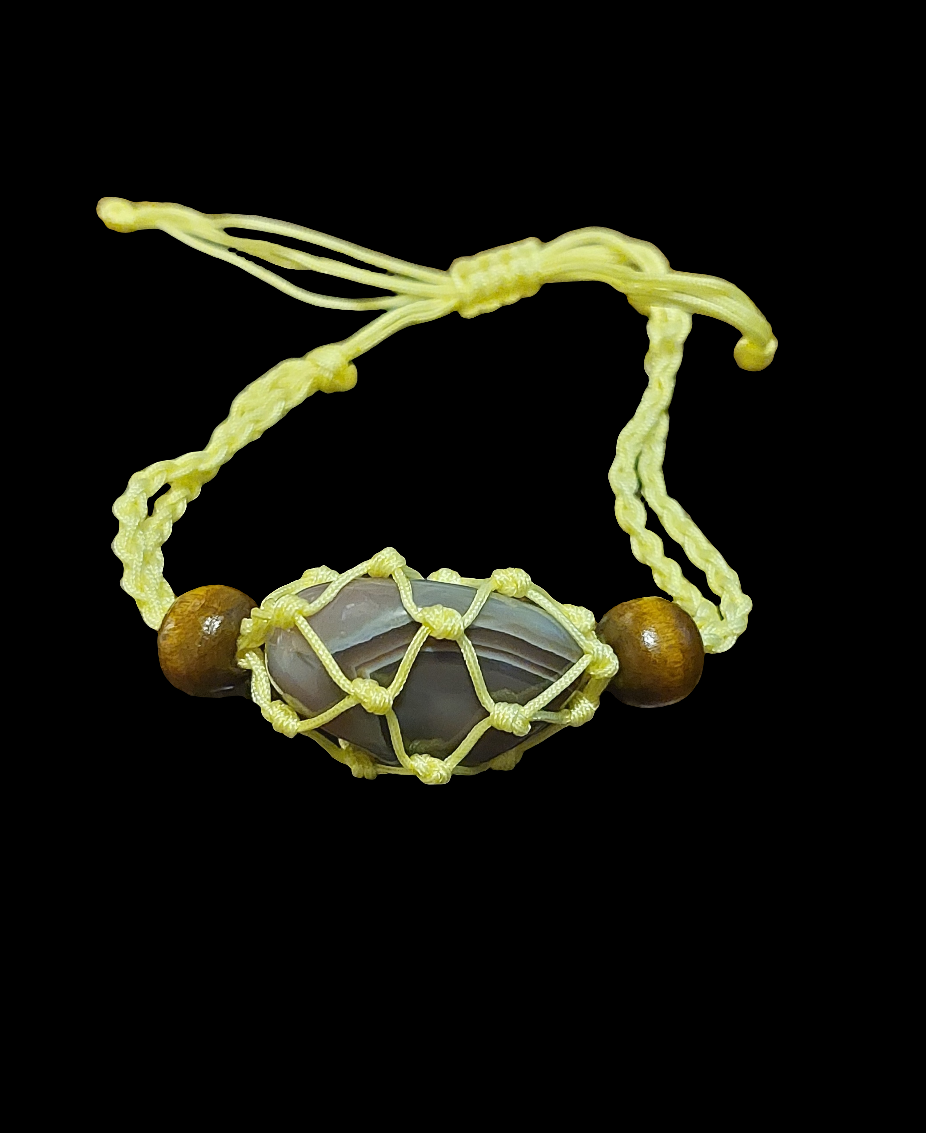 A yellow Macrame tumbled stone bracelet displayed on a clear stand against a beige background.