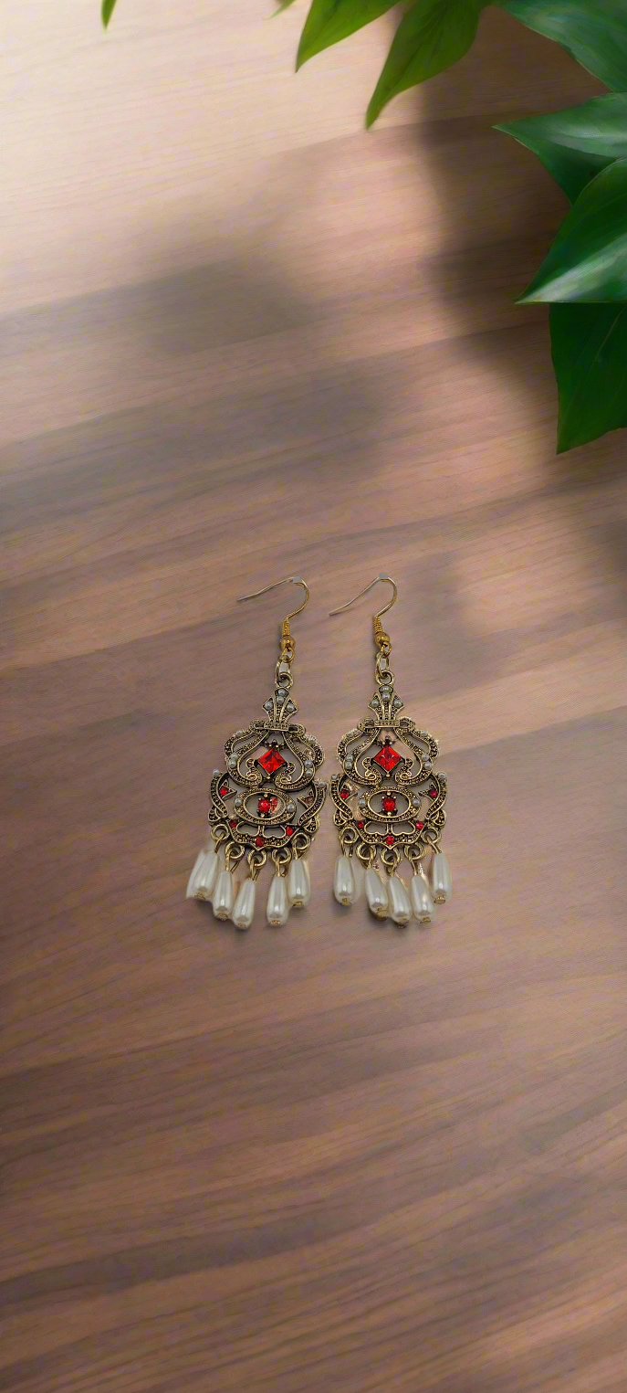 A pair of elegant earrings with intricate details and pearls, displayed against a wooden background.