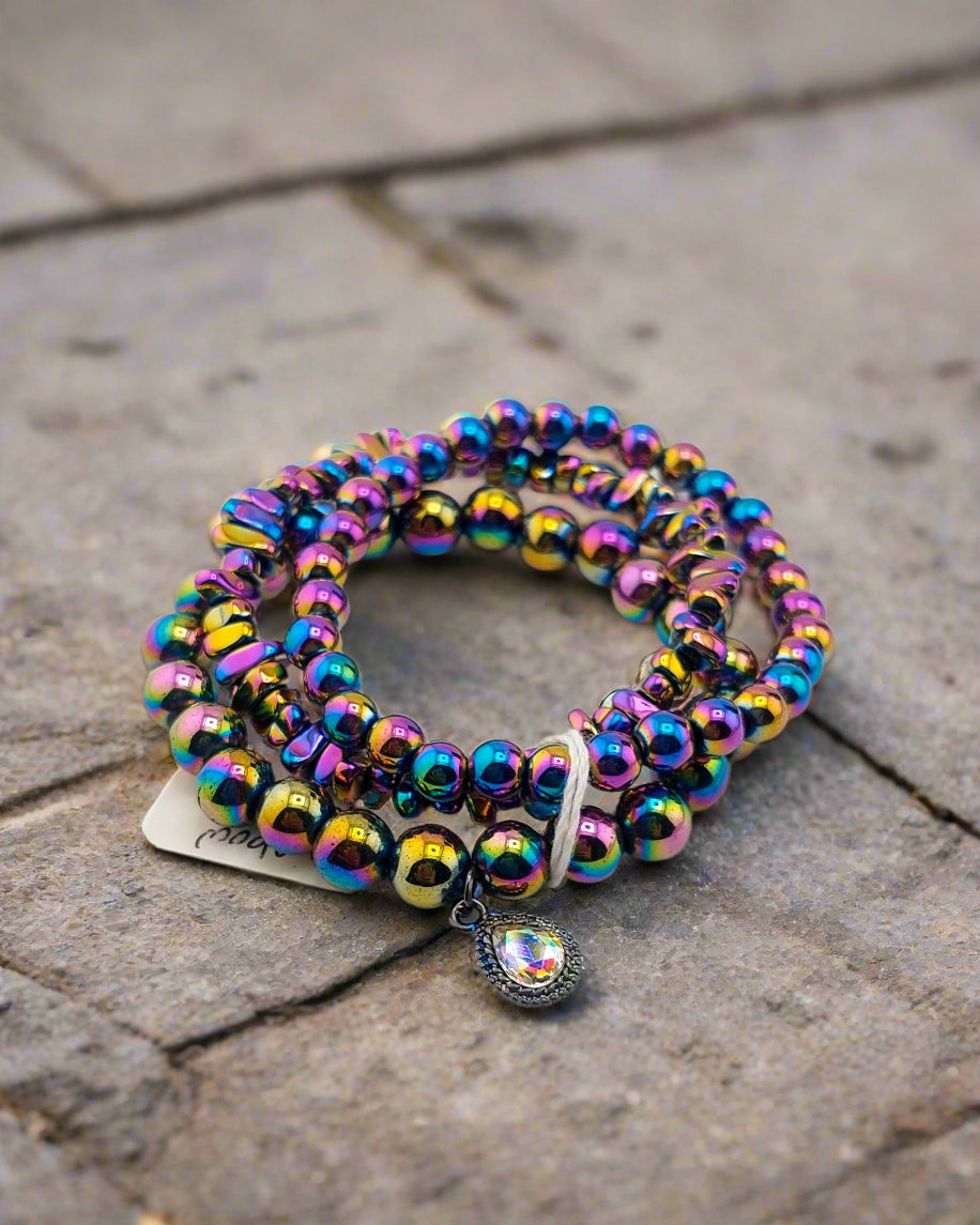 A multicolored rainbow hematite triple stack bracelet laid out on a textured surface.