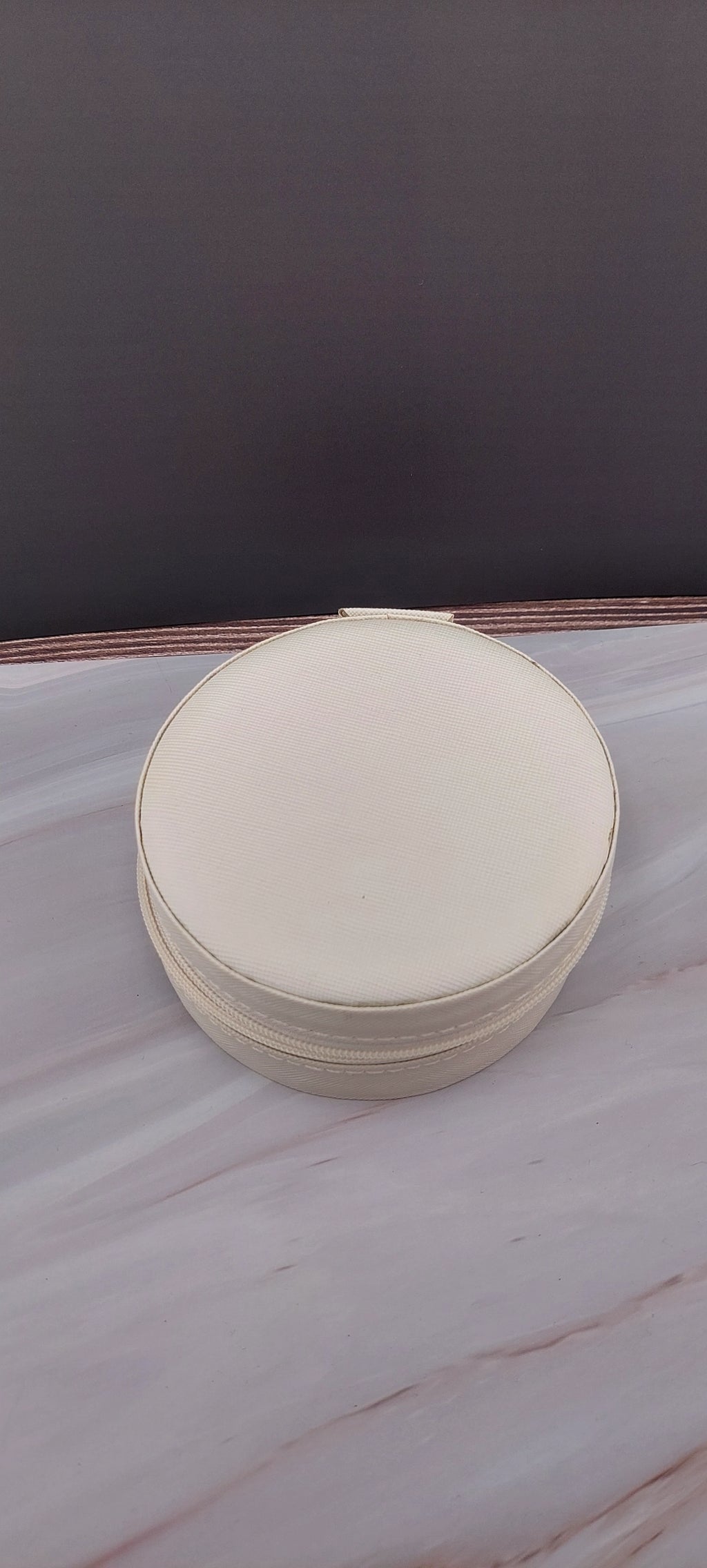 A round jewelry box with a beige interior and patterned exterior, partially open, showing its compartments.