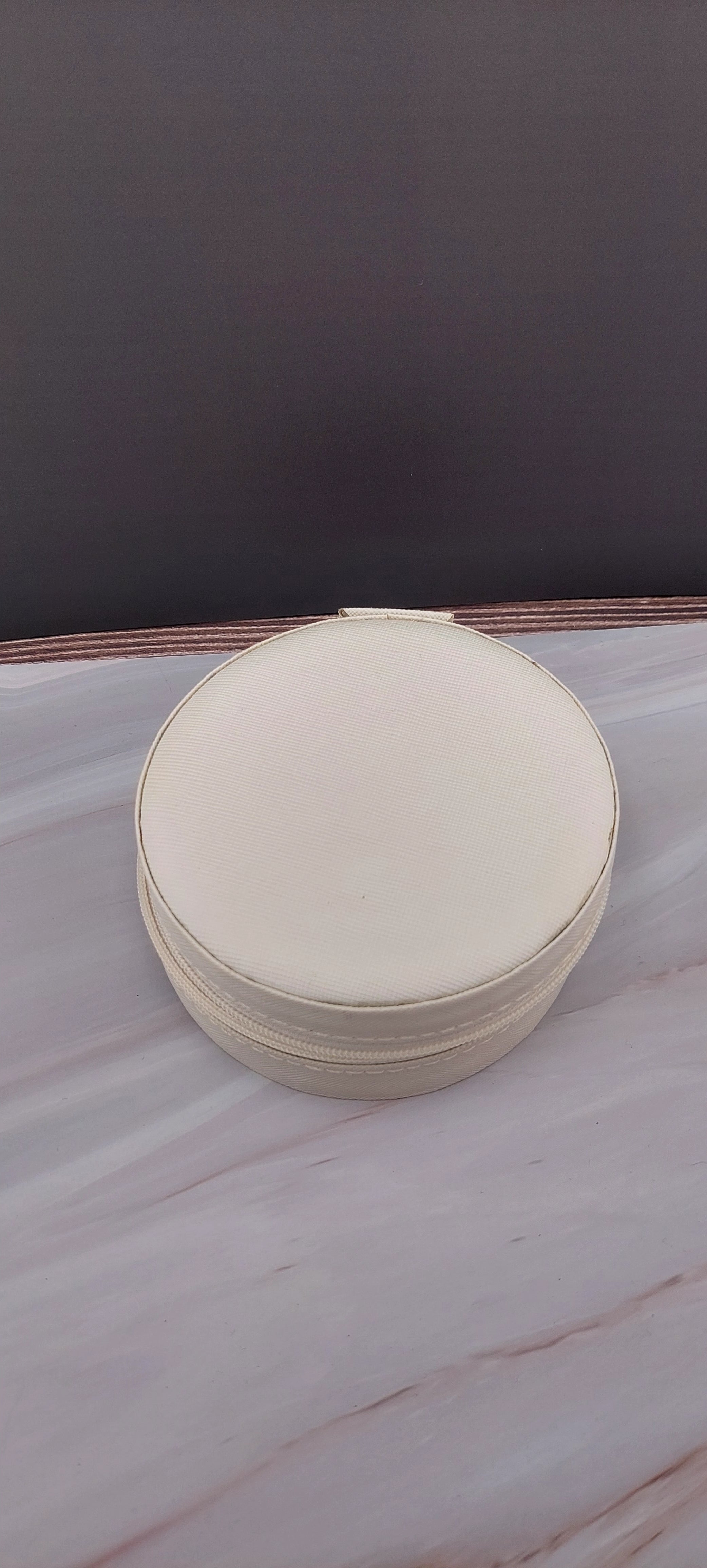 A round jewelry box with a beige interior and patterned exterior, partially open, showing its compartments.