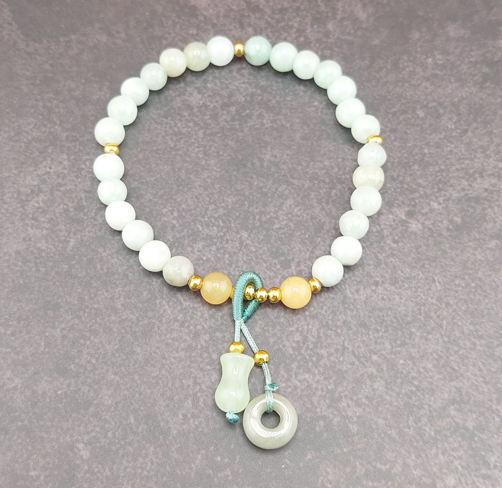 A bracelet made of round blue water jade stones with gold accents and a blue fabric tie at the clasp, featuring a small circular silver charm.