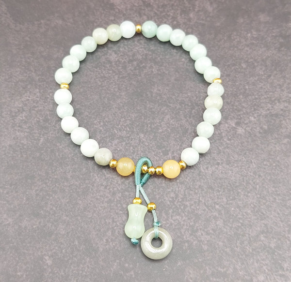 A bracelet made of round blue water jade stones with gold accents and a blue fabric tie at the clasp, featuring a small circular silver charm.