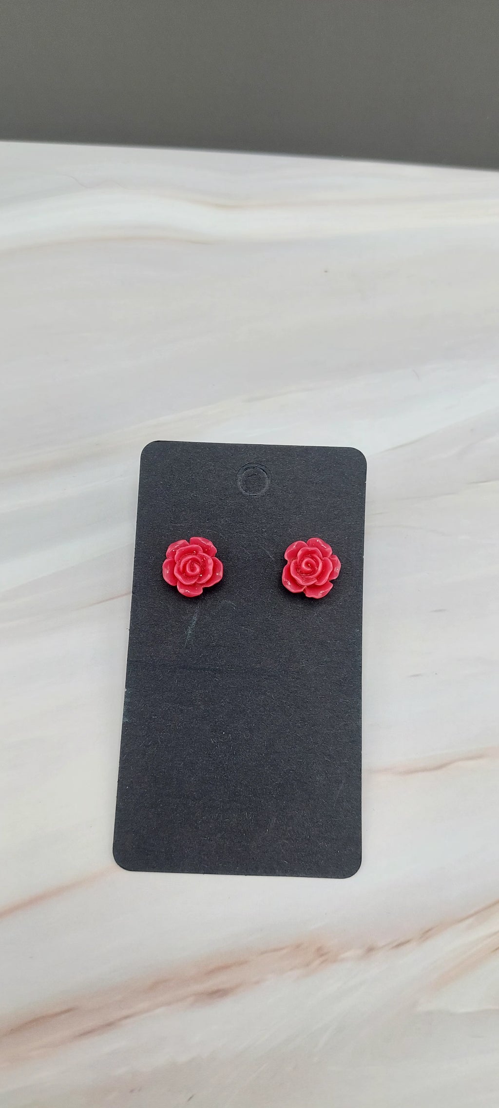 A pair of gold-colored rose stud earrings displayed on a black backing card.