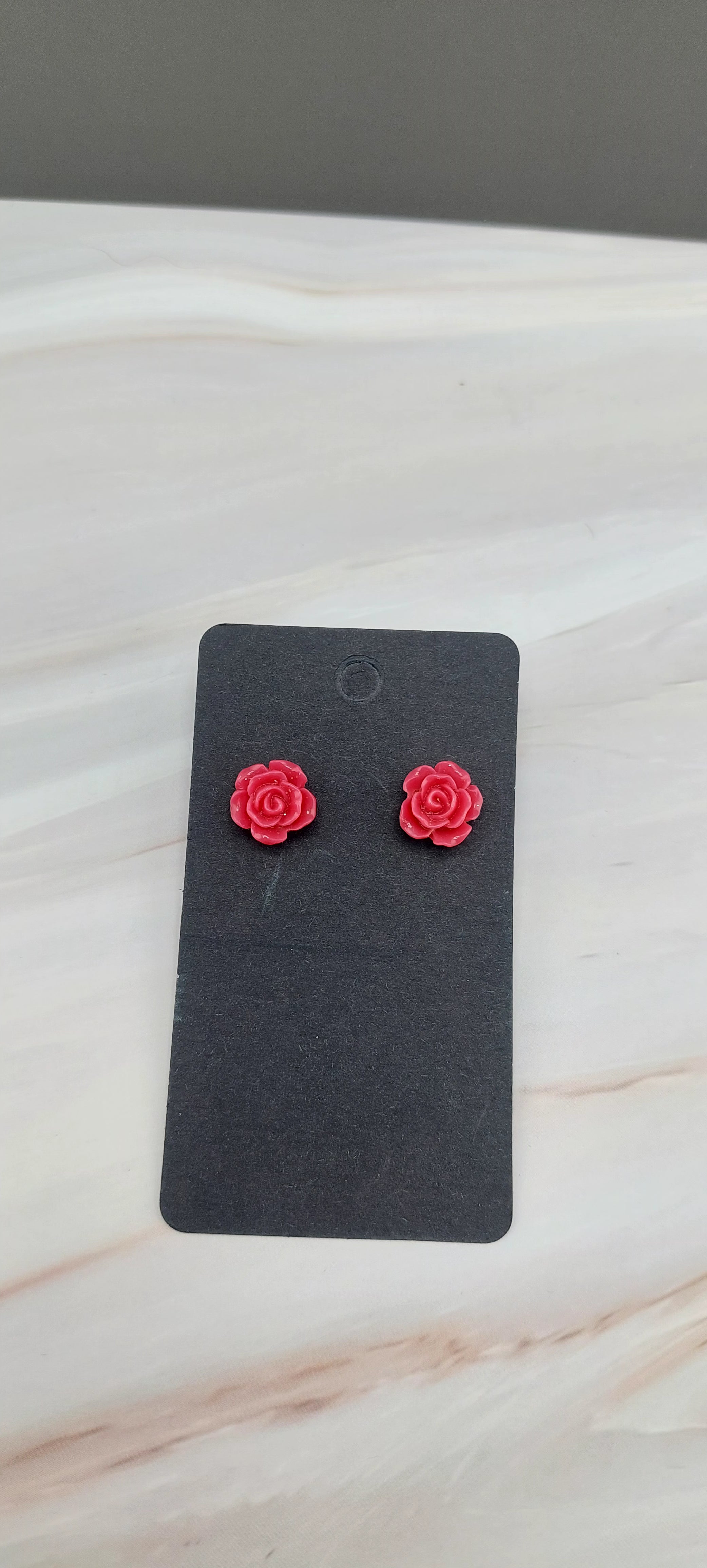 A pair of gold-colored rose stud earrings displayed on a black backing card.