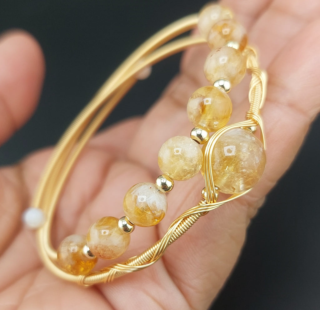 Gold bracelet with yellow beads held in a hand against a dark background