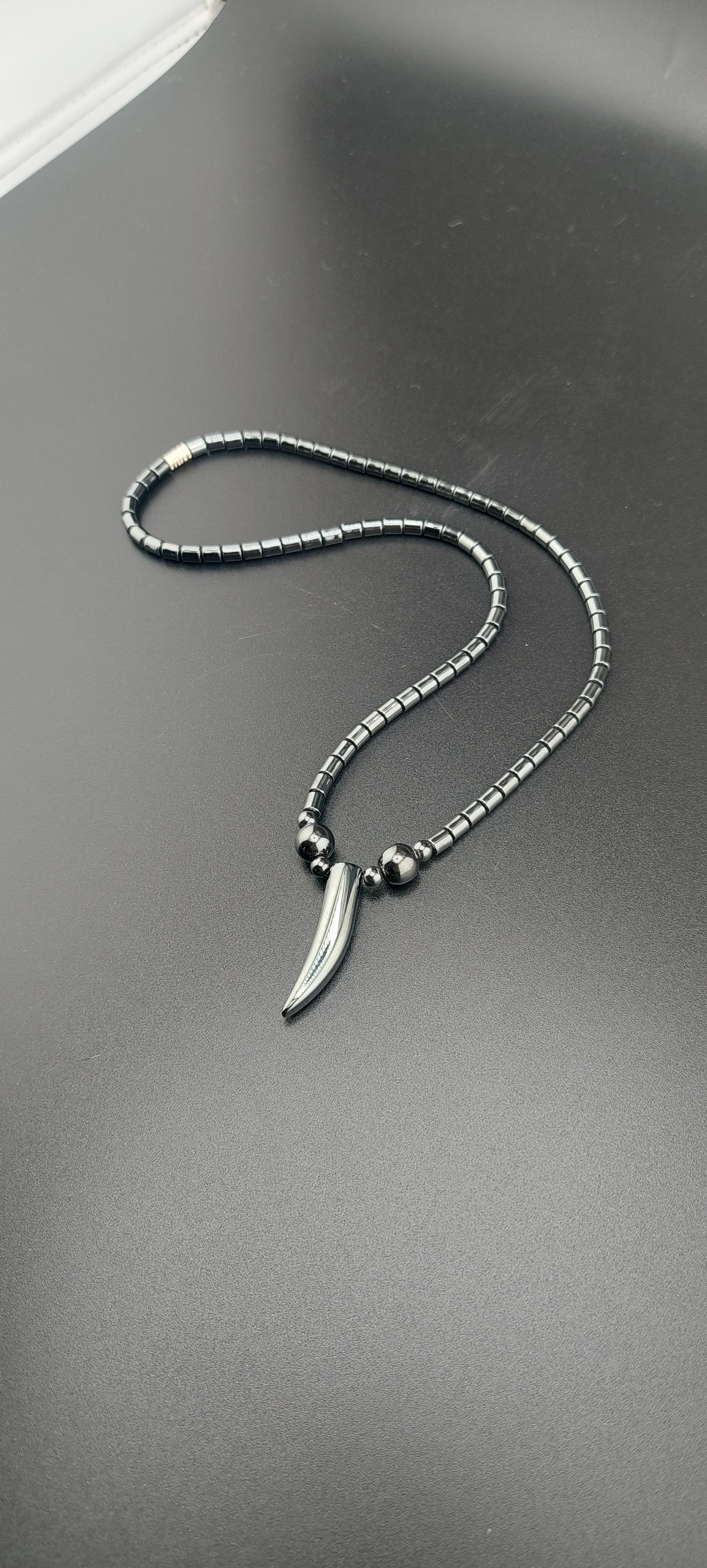 A silver-colored tooth-shaped necklace on a chain, displayed against a grey background.
