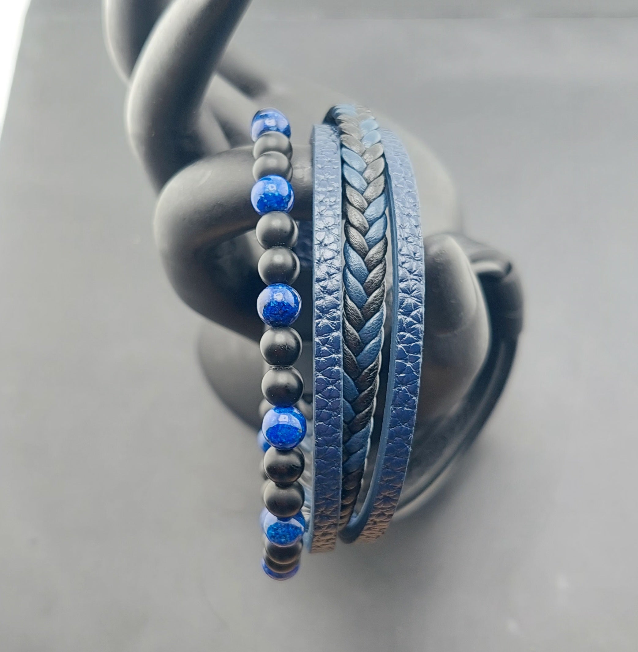 Three bracelets with blue beads and braided design on a gray stand.
