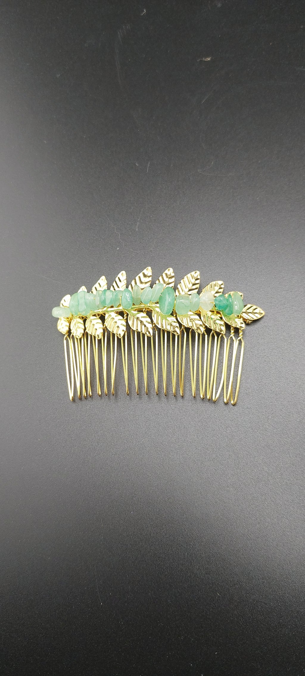 A collection of gold leaf hair clips with various colored stones attached to them, displayed against a dark background.