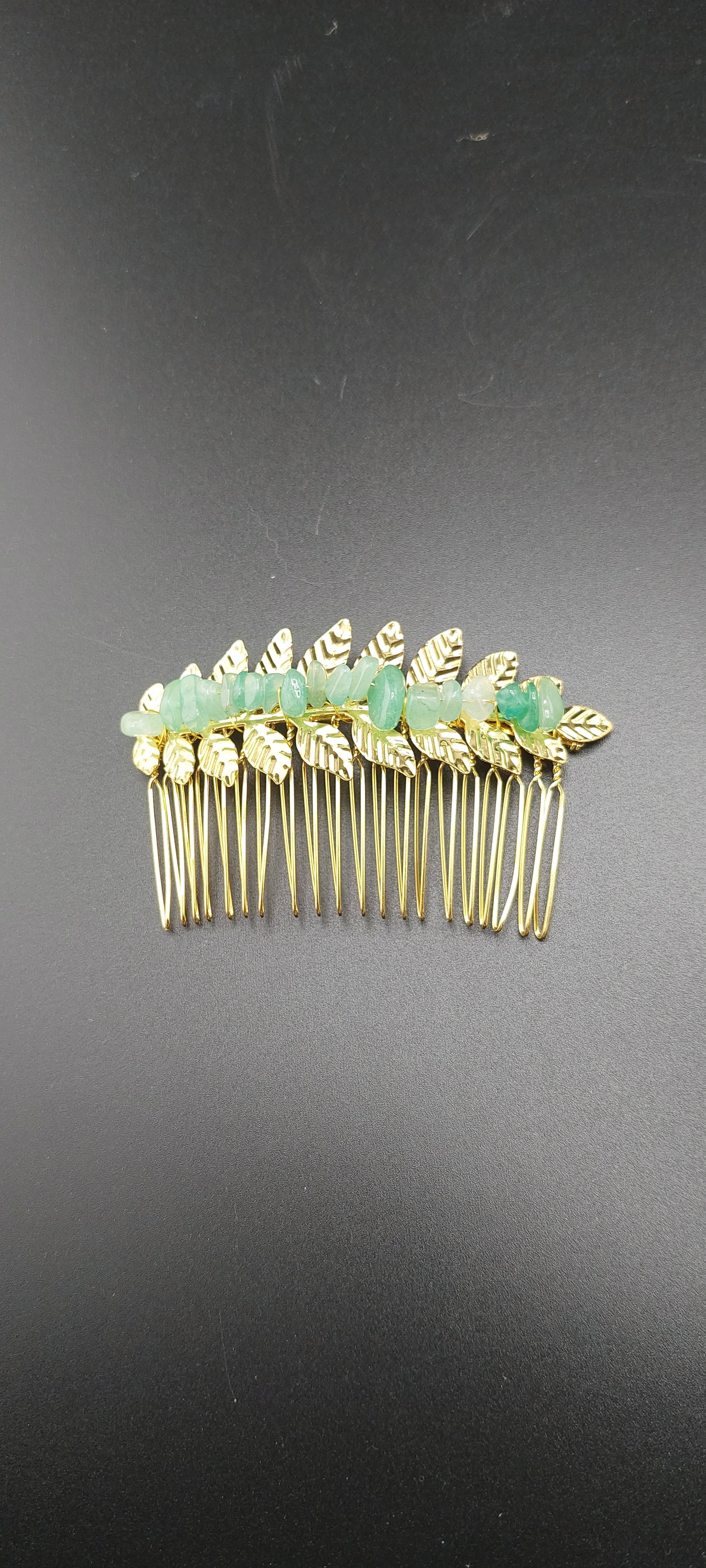 A collection of gold leaf hair clips with various colored stones attached to them, displayed against a dark background.