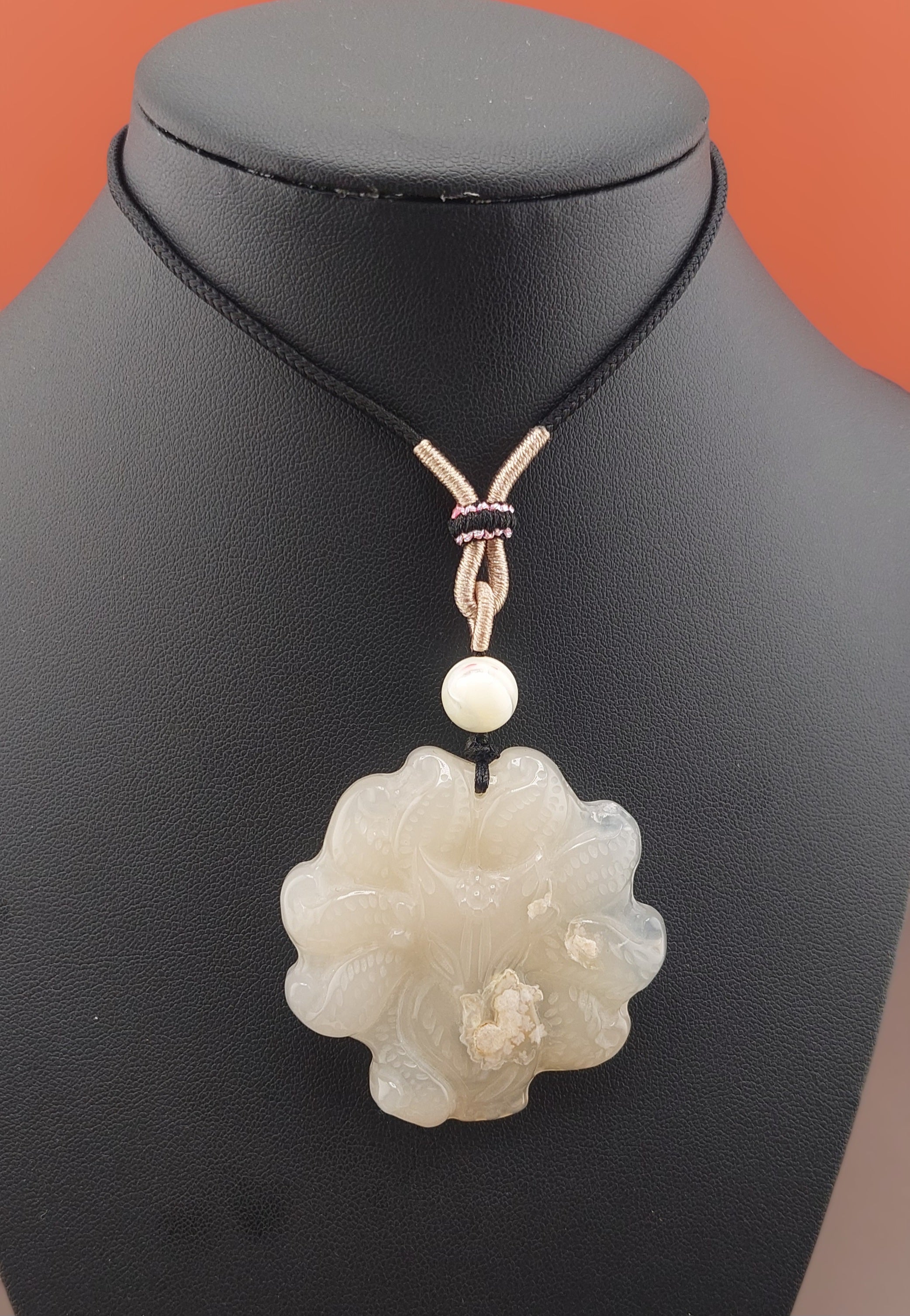 A white flower-shaped agate necklace displayed on a black mannequin against an orange background, featuring a small white bead and a metal clasp.
