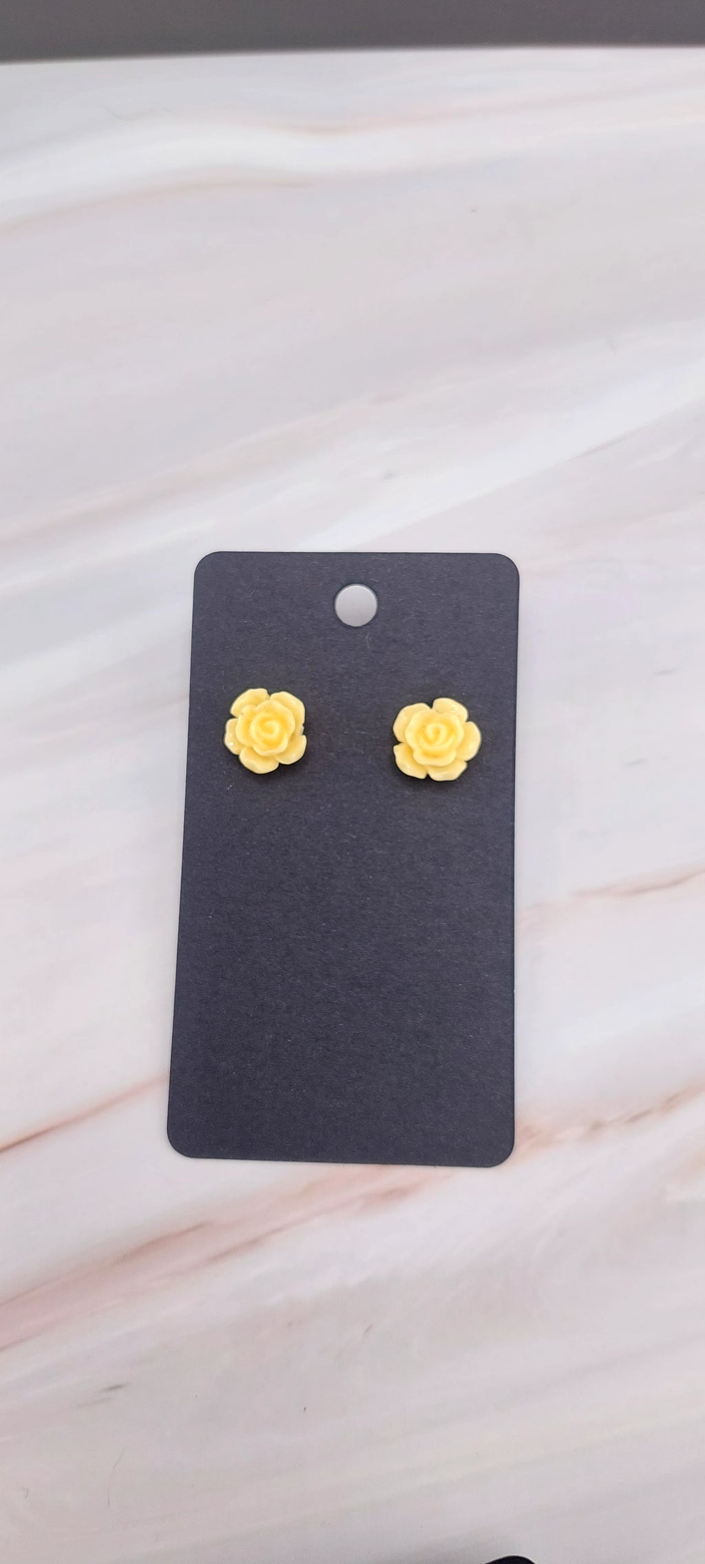 A pair of gold-colored rose stud earrings displayed on a black backing card.