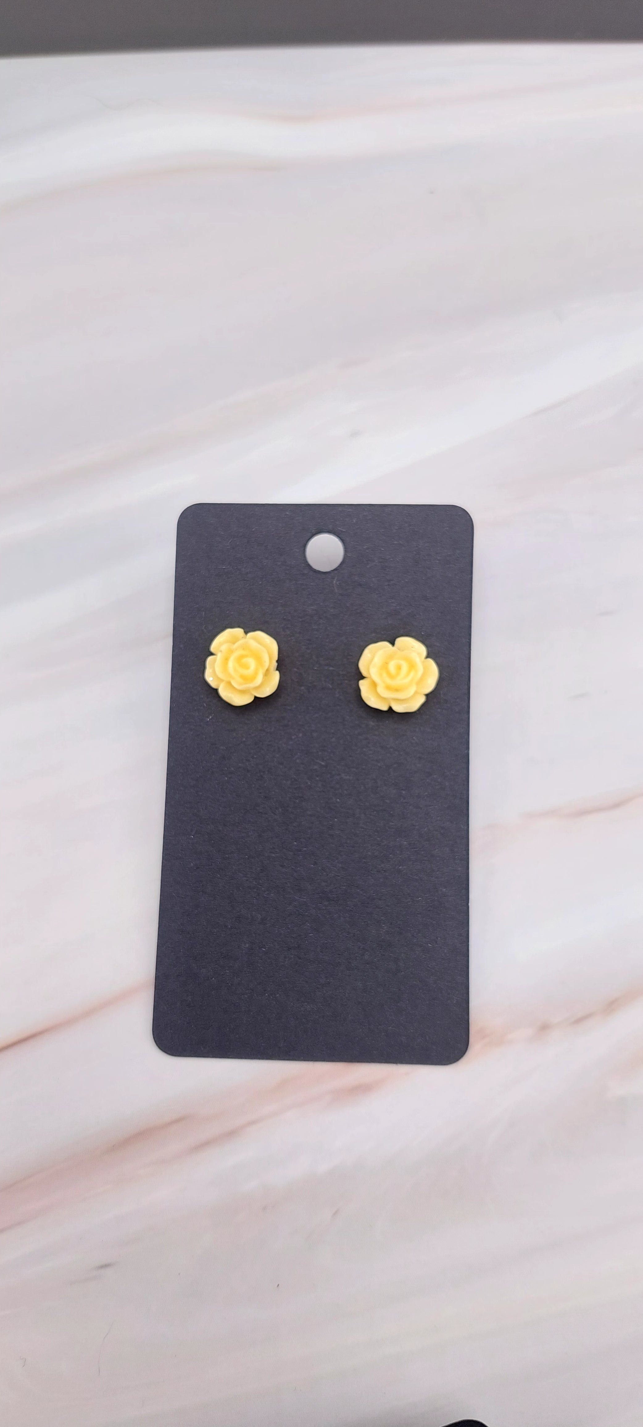 A pair of gold-colored rose stud earrings displayed on a black backing card.