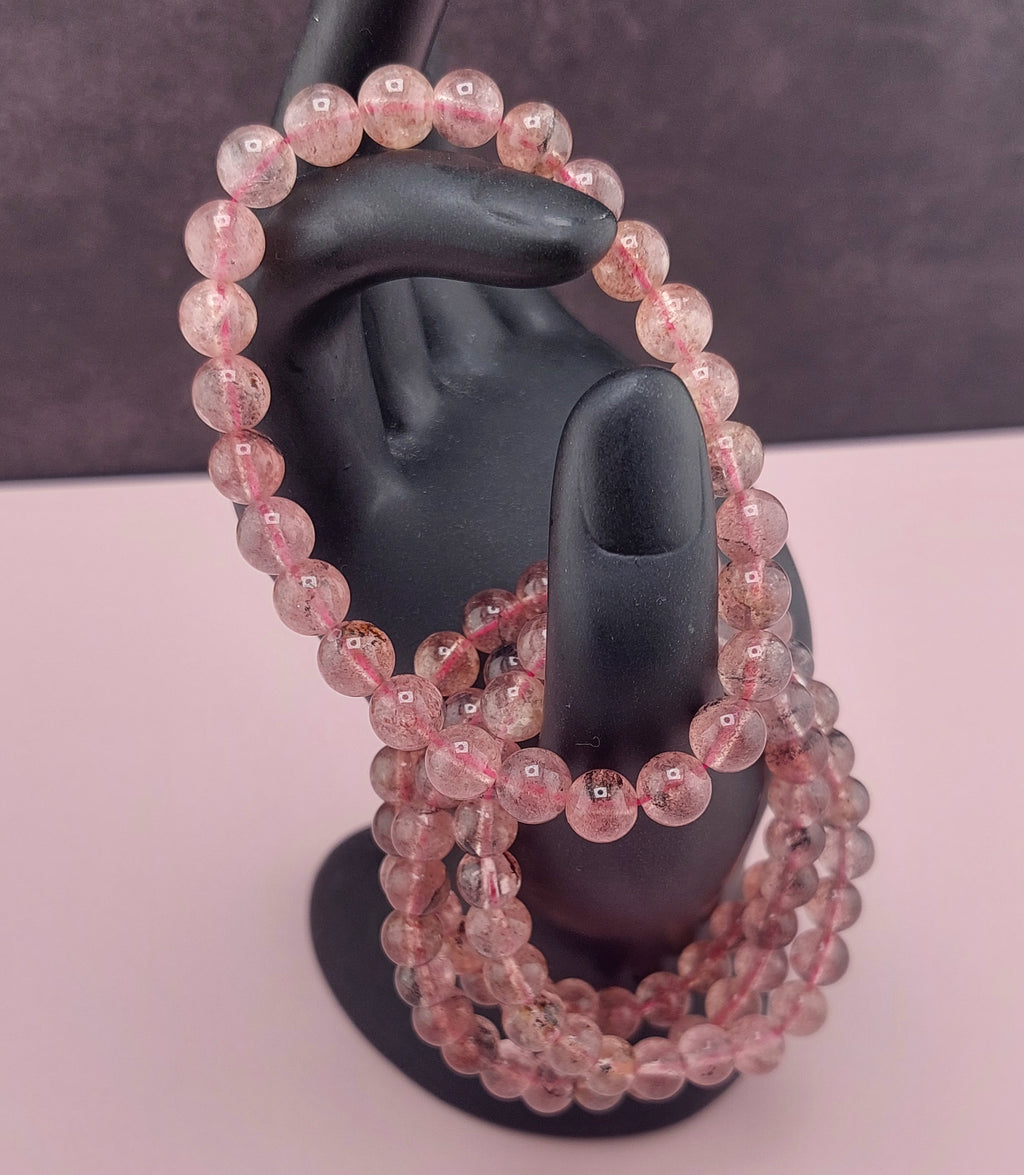 Pink beaded bracelets on a black mannequin hand against a dark background