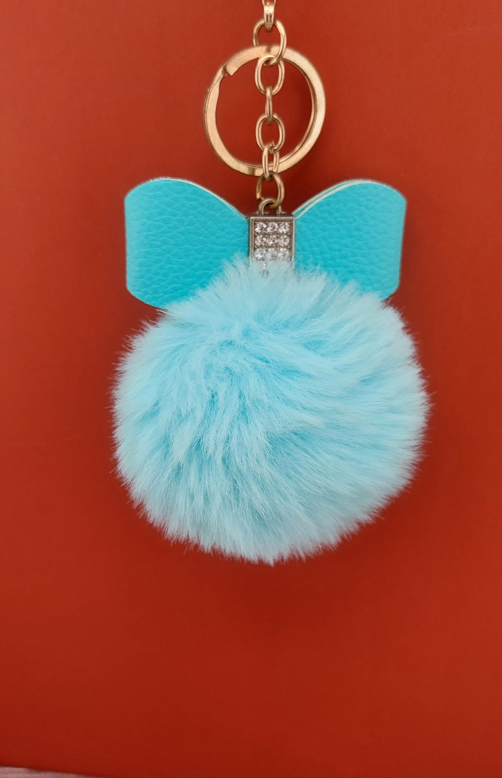 Blue pom-pom keychain with bow on a red background