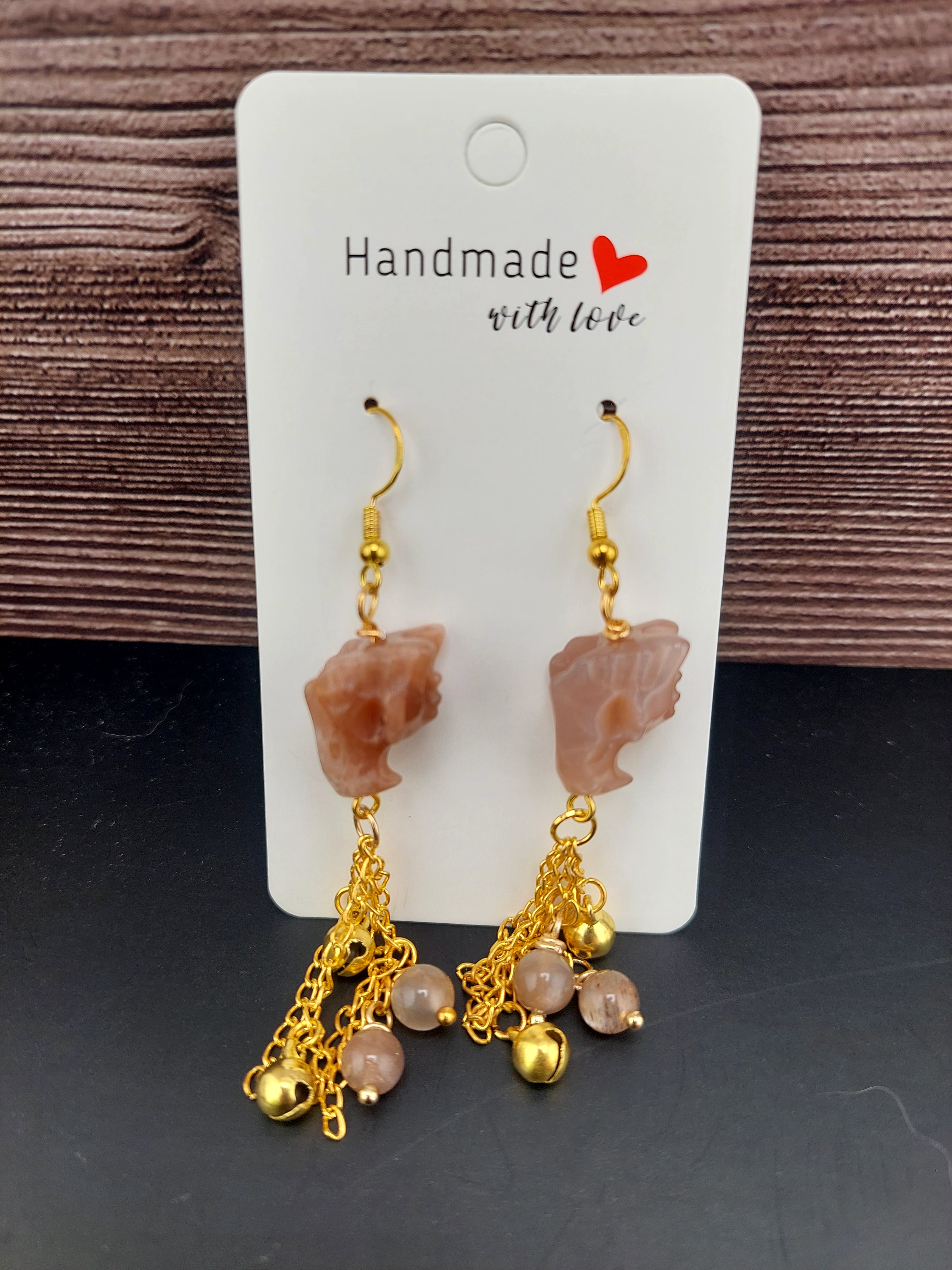 Pair of gold and stone earrings on a 'Handmade with Love' card against a wooden background.