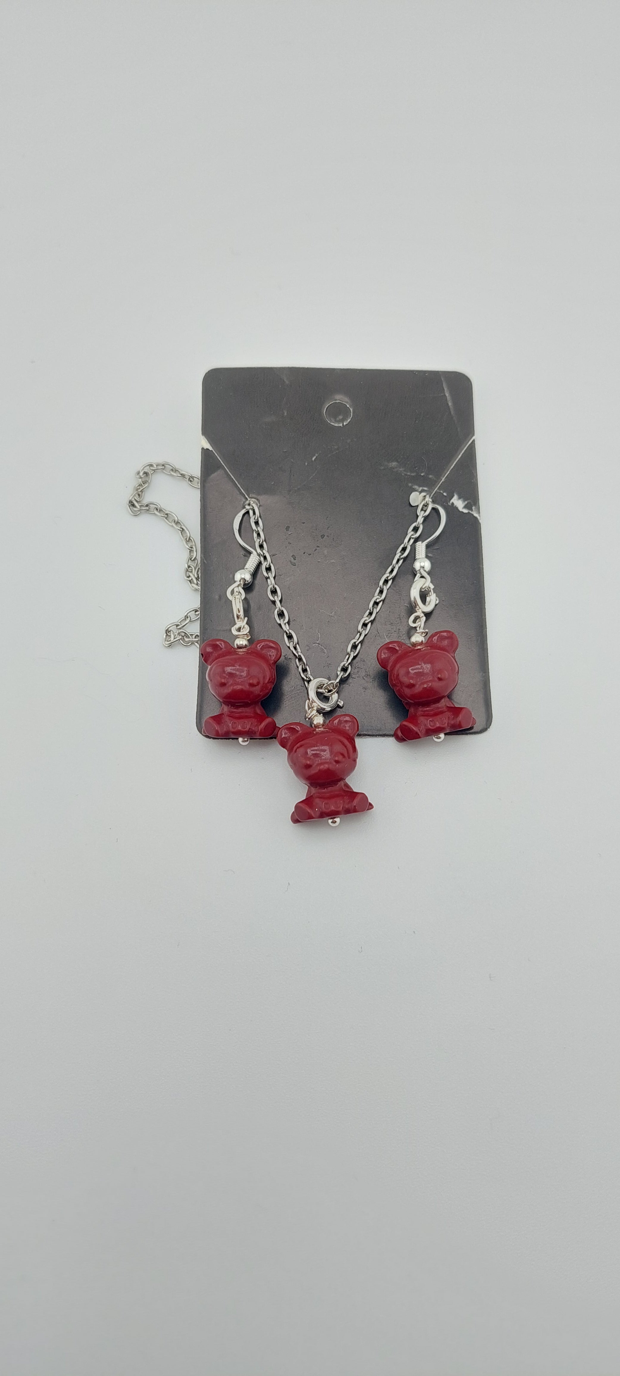 A set of jewelry featuring red cinnabar stones shaped like Mickey Mouse heads, including a bracelet and a pair of earrings, displayed on a black card.