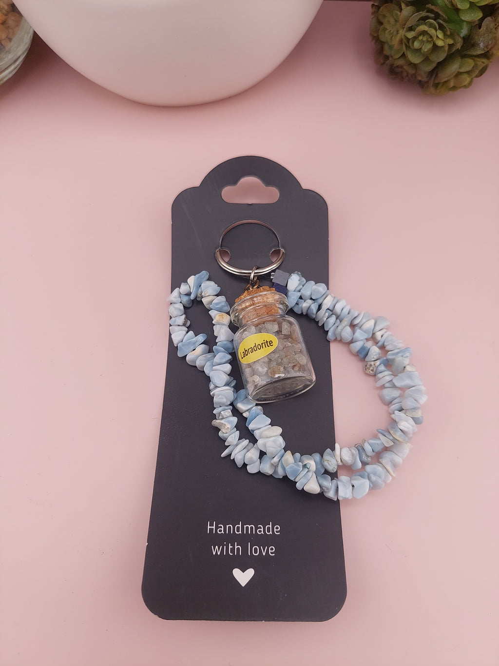 Keychain with stones on a black card labeled 'Handmade with love' on a pink background