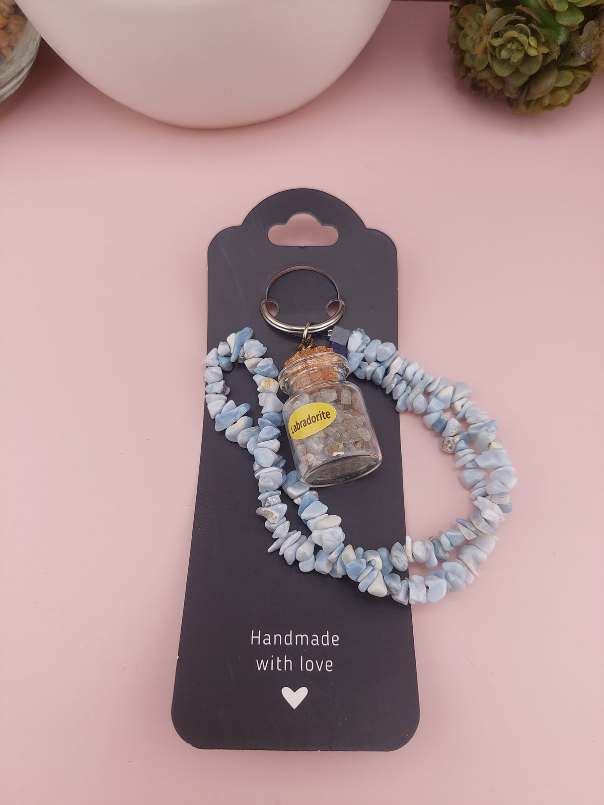 Keychain with stones on a black card labeled 'Handmade with love' on a pink background