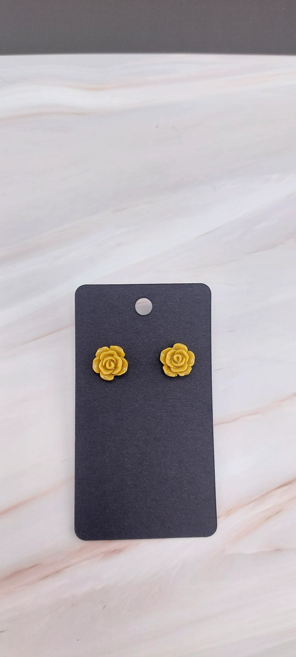 A pair of gold-colored rose stud earrings displayed on a black backing card.